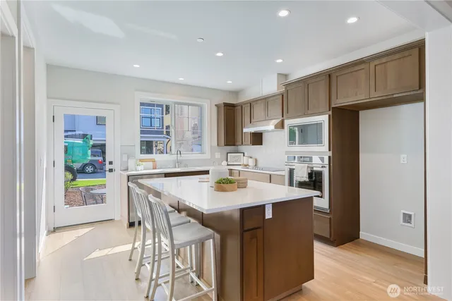 a kitchen with stainless steel appliances kitchen island granite countertop a refrigerator a sink a stove a dining table and chairs