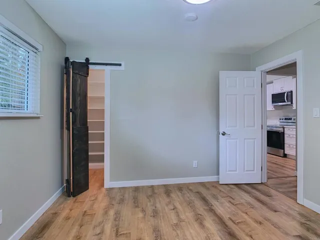 a view of an empty room with wooden floor and kitchen