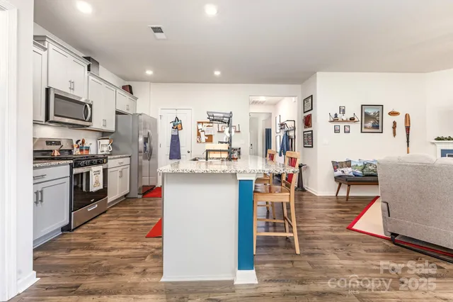 a kitchen with stainless steel appliances granite countertop a stove top oven a sink a dining table and chairs with wooden floor