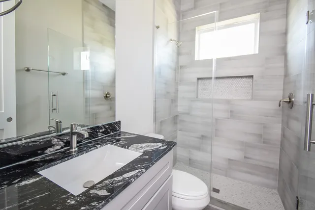 a bathroom with a granite countertop sink toilet a mirror and shower