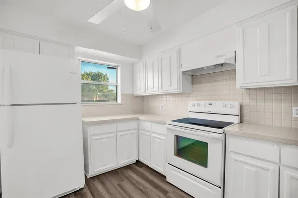 a kitchen with cabinets appliances wooden floor and a window