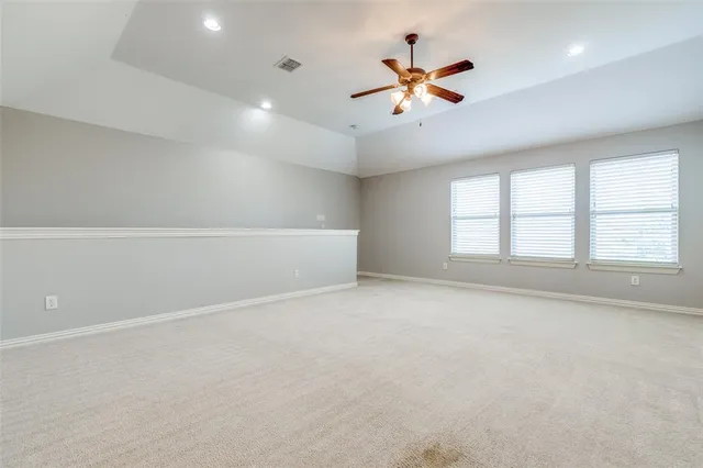 an empty room with ceiling fan and windows