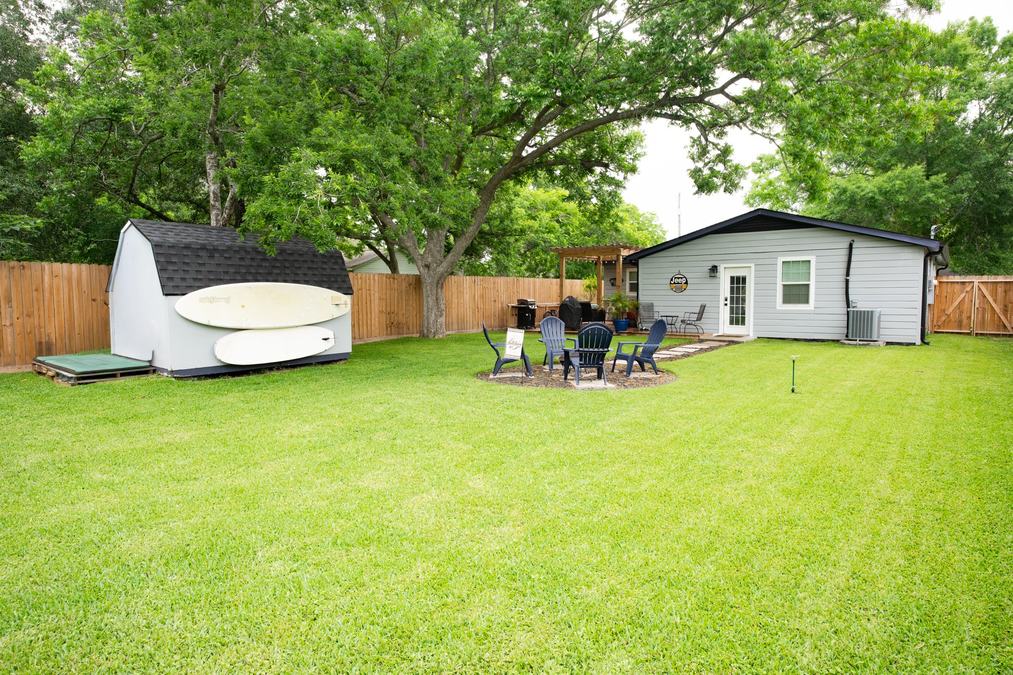 846 South Anderson Street Angleton, TX 77515 - Photo 27 of 30 Spacious backyard with lush green lawn and mature trees. Features a cozy fire pit area with seating, a storage shed, and a charming patio for outdoor dining. Ideal for relaxation and entertainment.