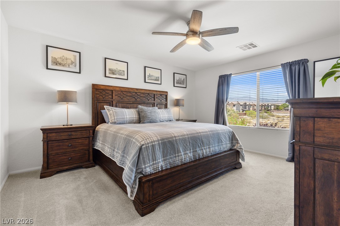 891 Earth Luster Road Las Vegas, NV 89178 - Photo 11 of 48 Relax in this well-lit primary bedroom featuring a ceiling fan, plush carpet, and a large window overlooking the neighborhood.