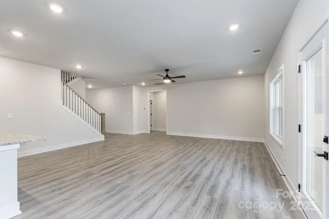 a view of an empty room with wooden floor and a kitchen