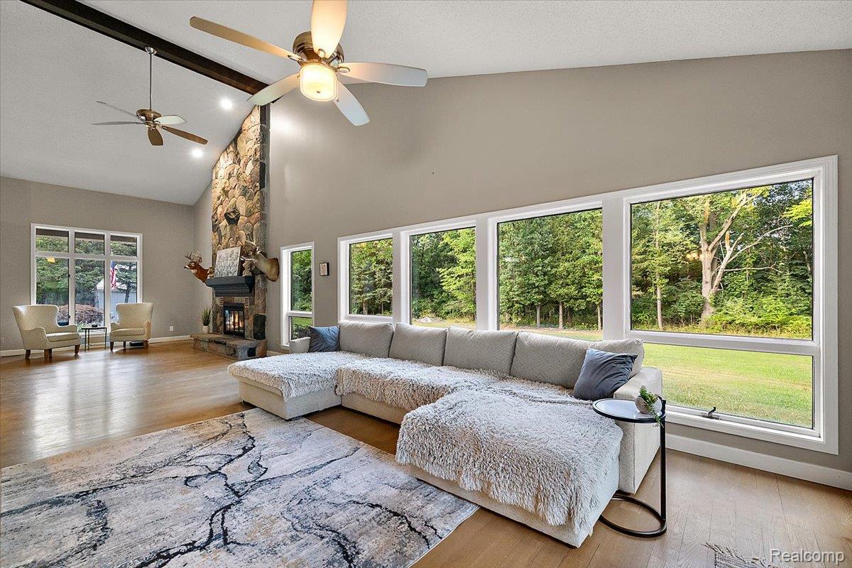 707 West Sutton Road Metamora, MI 48455 - Photo 28 of 84 Expansive living area featuring vaulted ceilings, wood-finish flooring, a stone-clad fireplace, and large windows