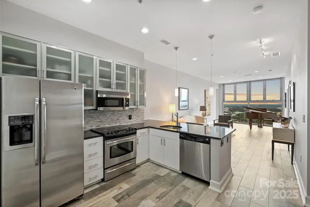 a kitchen with stainless steel appliances granite countertop a stove top oven a sink dishwasher a refrigerator and white cabinets with wooden floor