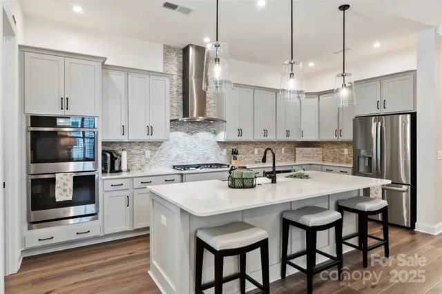 a kitchen with stainless steel appliances a stove a sink a refrigerator a center island and chairs