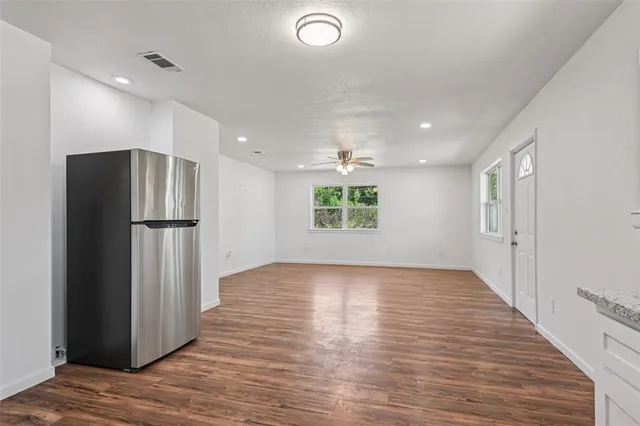 a view of an empty room with wooden floor and a kitchen