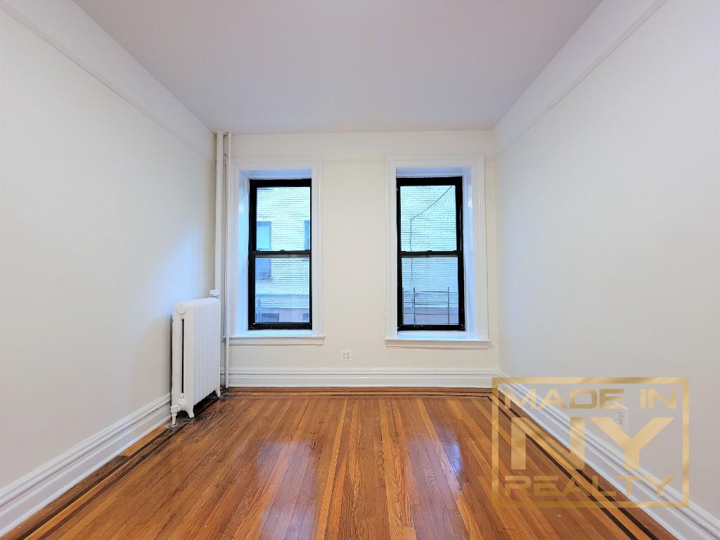 29-07 31st Avenue, Unit 1E Queens, NY 11106 - Photo 3 of 7 an empty room with wooden floor and windows