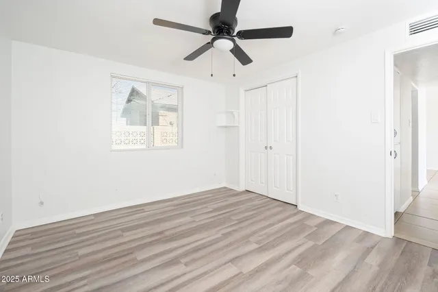 an empty room with wooden floor ceiling fan and windows
