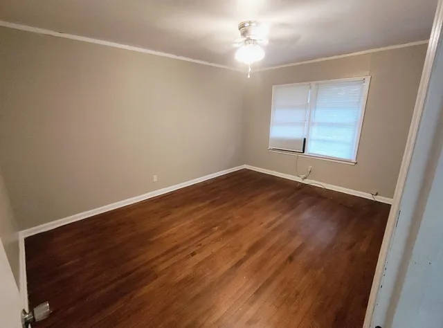 an empty room with wooden floor chandelier fan and windows