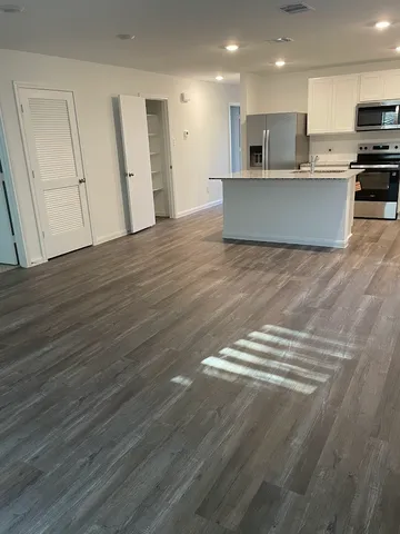 a view of kitchen with stainless steel appliances wooden floor and living room