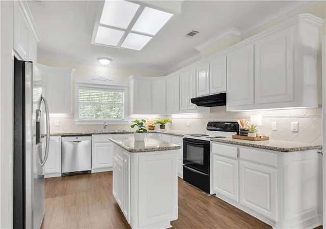 a kitchen with stainless steel appliances granite countertop a stove a sink dishwasher a refrigerator white cabinets and wooden floor