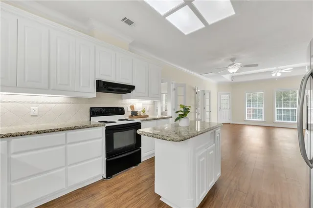 a kitchen with granite countertop a stove top oven a sink dishwasher and white cabinets with wooden floor