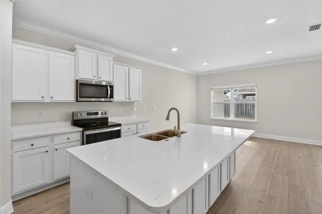 a kitchen with stainless steel appliances a microwave a stove a sink dishwasher a refrigerator and white cabinets with wooden floor