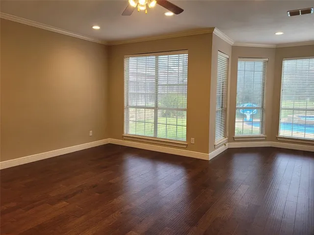 an empty room with wooden floor and windows with curtains