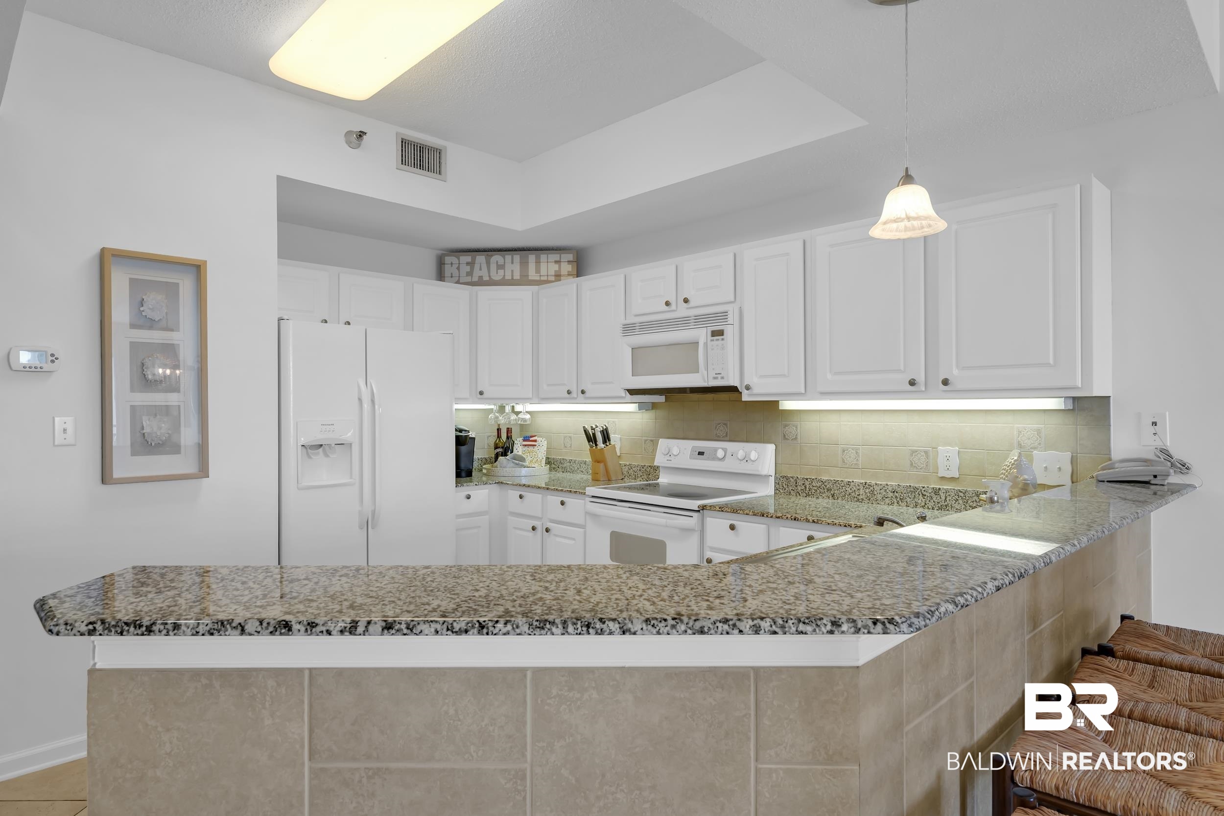 27282 Canal Road, Unit 104 Orange Beach, AL 36561 - Photo 18 of 79 Kitchen featuring white appliances, a peninsula, backsplash, hanging light fixtures, and light stone countertops