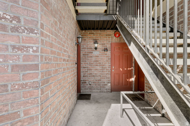 8264 South Resaca Drive, Unit K3 Sandy, UT 84070 - Photo 3 of 30 Brick exterior featuring a red entry door, sconce lighting, concrete walkway, and a metal staircase with railing