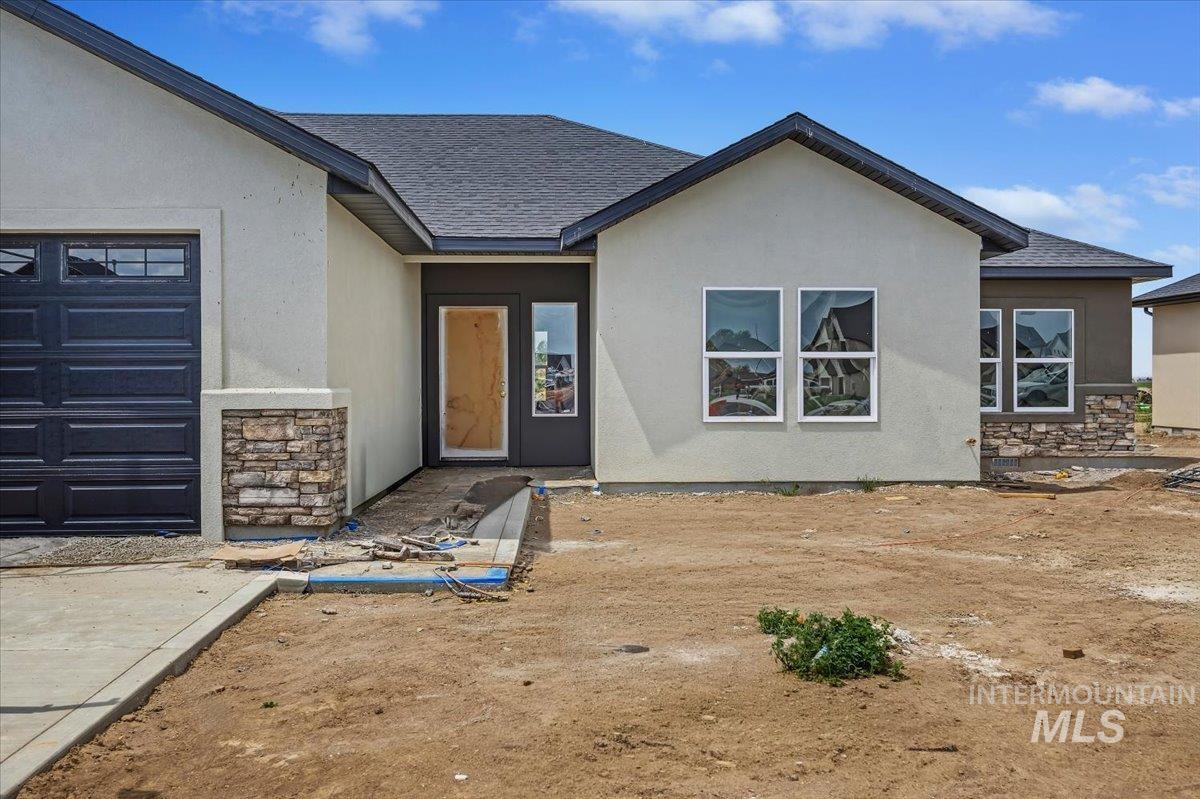 1121 Moss Rupert, ID 83350 - Photo 2 of 2 Exterior showcasing stucco siding, dark roof shingles, an attached garage with a dark panel door, and decorative stacked stone accents