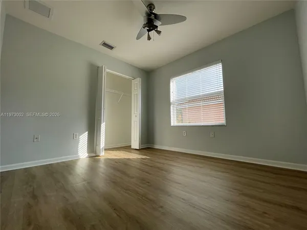 an empty room with wooden floor chandelier fan and windows