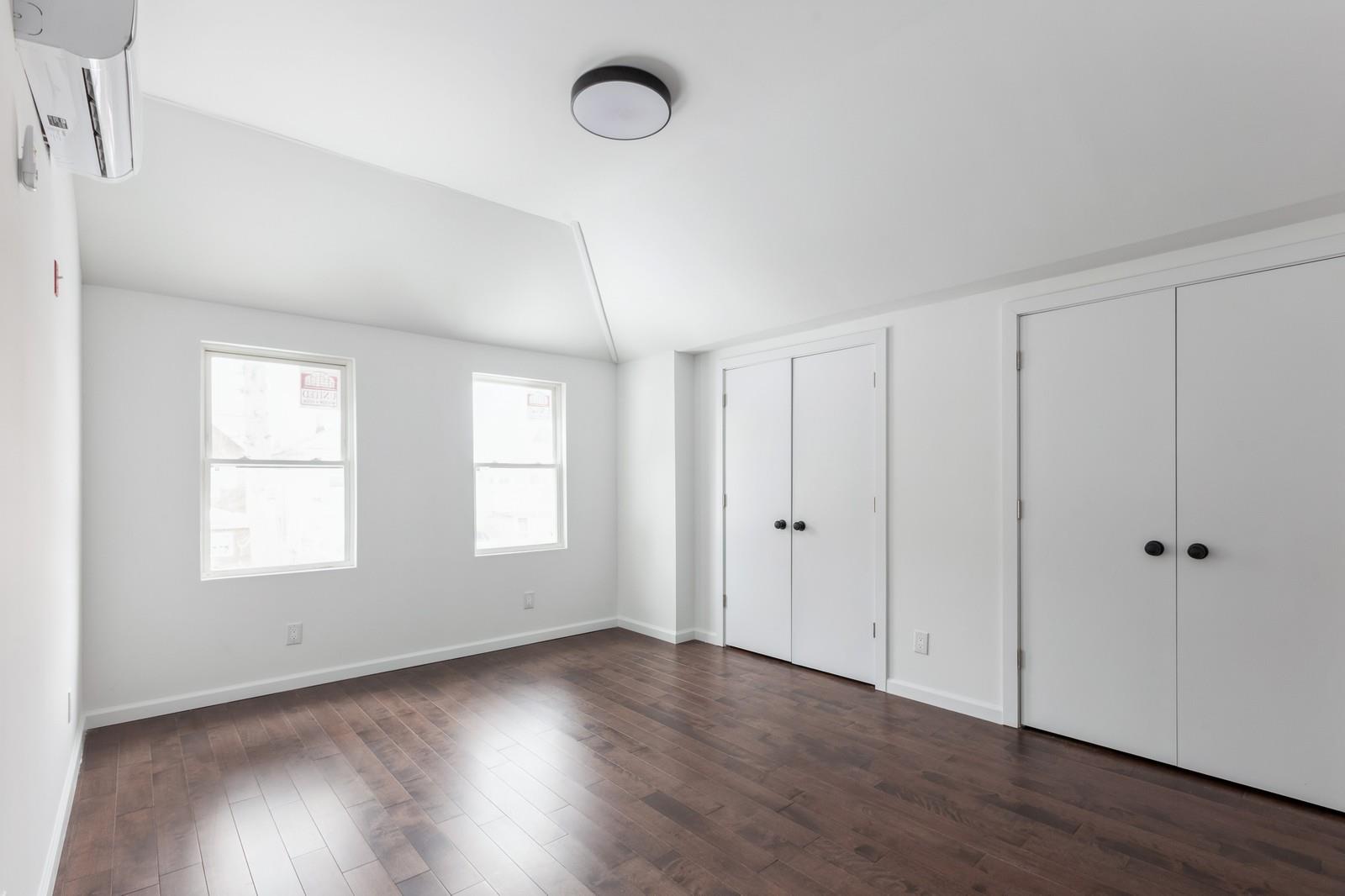 100-03 90th Avenue Queens, NY 11418 - Photo 14 of 18 Unfurnished bedroom with vaulted ceiling, a wall unit AC, dark wood finished floors, multiple closets, and baseboards
