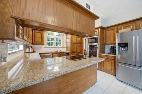 a kitchen with stainless steel appliances granite countertop a refrigerator a stove and a sink with wooden floors