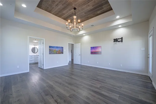 an empty room with wooden floor chandelier and windows