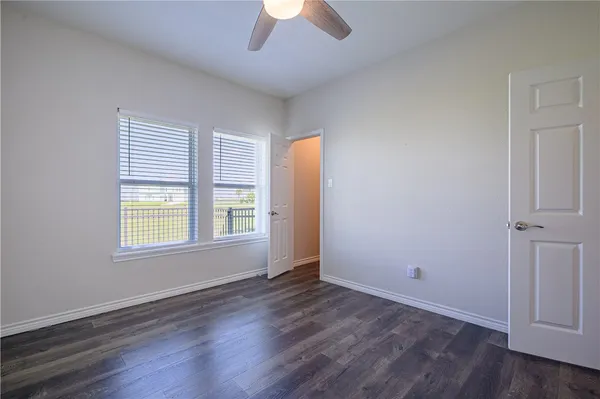 an empty room with wooden floor chandelier fan and windows