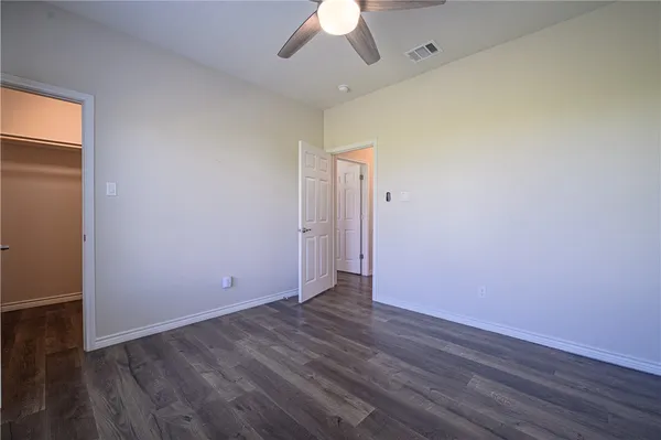 an empty room with wooden floor chandelier fan and windows