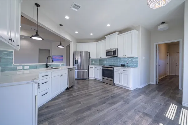 a large kitchen with granite countertop a large counter top a sink stainless steel appliances and cabinets