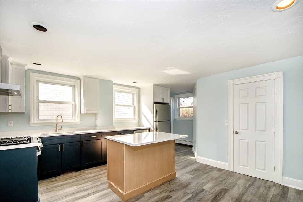 7 Whitehead Avenue, Unit 1 Hull, MA 02045 - Photo 6 of 32 a large white kitchen with granite countertop a sink and dishwasher a stove with wooden floors