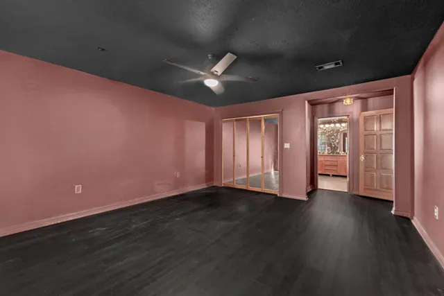 a view of an empty room with wooden floor and a ceiling fan