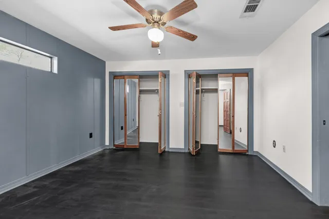 an empty room with wooden floor chandelier fan and windows