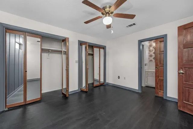 a view of an empty room with wooden floor and a ceiling fan