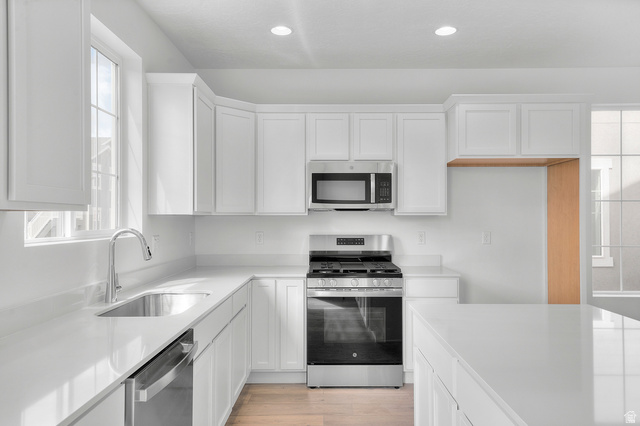 7797 West Alta Springs Way Magna, UT 84044 - Photo 12 of 21 Kitchen featuring appliances with stainless steel finishes, white cabinetry, light wood-style floors, recessed lighting, and light stone countertops