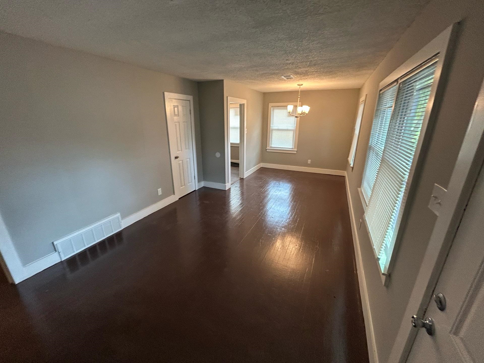 4824 Hodge Road Memphis, TN 38109 - Photo 4 of 6 Empty room featuring dark wood-type flooring, a textured ceiling, and an inviting chandelier