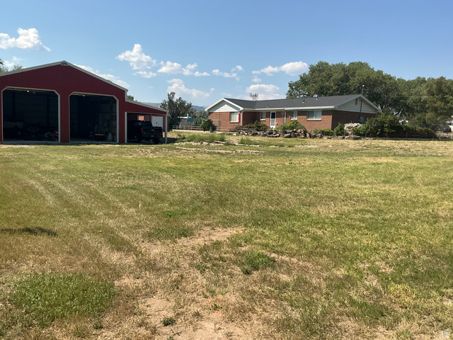 98 Main Street Manila, UT 84046 - Photo 27 of 36 Expansive lot featuring a red barn with open bays and a brick residence with a dark roof and mature trees