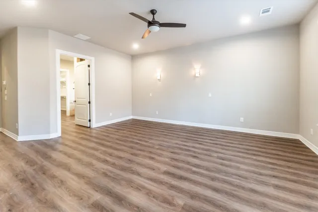 an empty room with wooden floor ceiling fan and windows