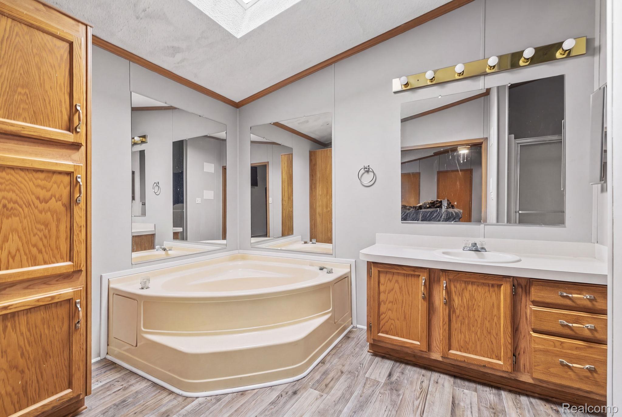 19921 Rhapsody Drive Clinton Township, MI 48036 - Photo 12 of 19 Corner soaking tub, wood-finish flooring, wood cabinetry with ample storage, integrated vanity sink with white countertop, and a skylight