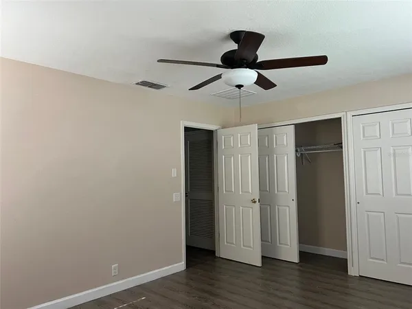 an empty room with wooden floor closet ceiling fan and windows