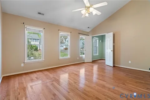an empty room with wooden floor chandelier fan and windows