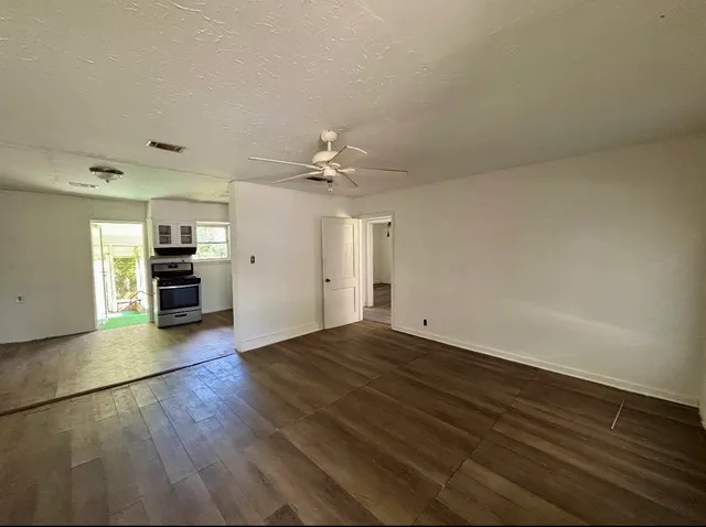 an empty room with wooden floor kitchen view and a window
