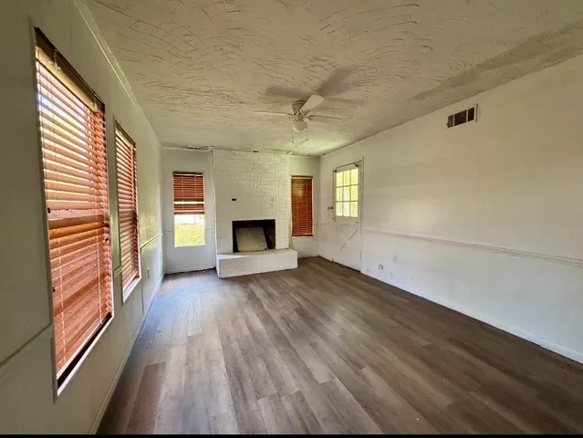 a view of an empty room with wooden floor fireplace and a window