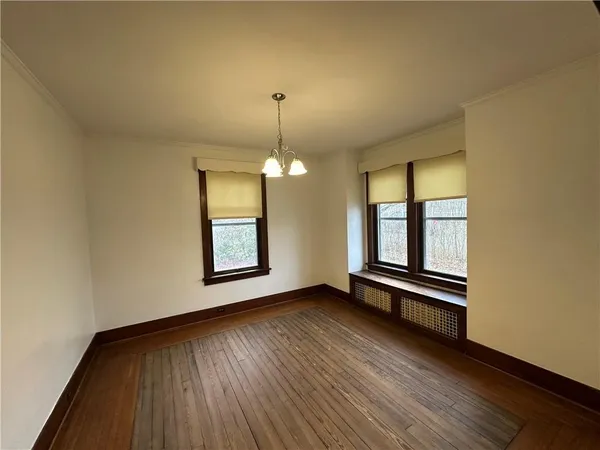 an empty room with wooden floor chandelier and windows
