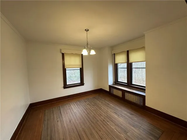 an empty room with wooden floor chandelier and windows