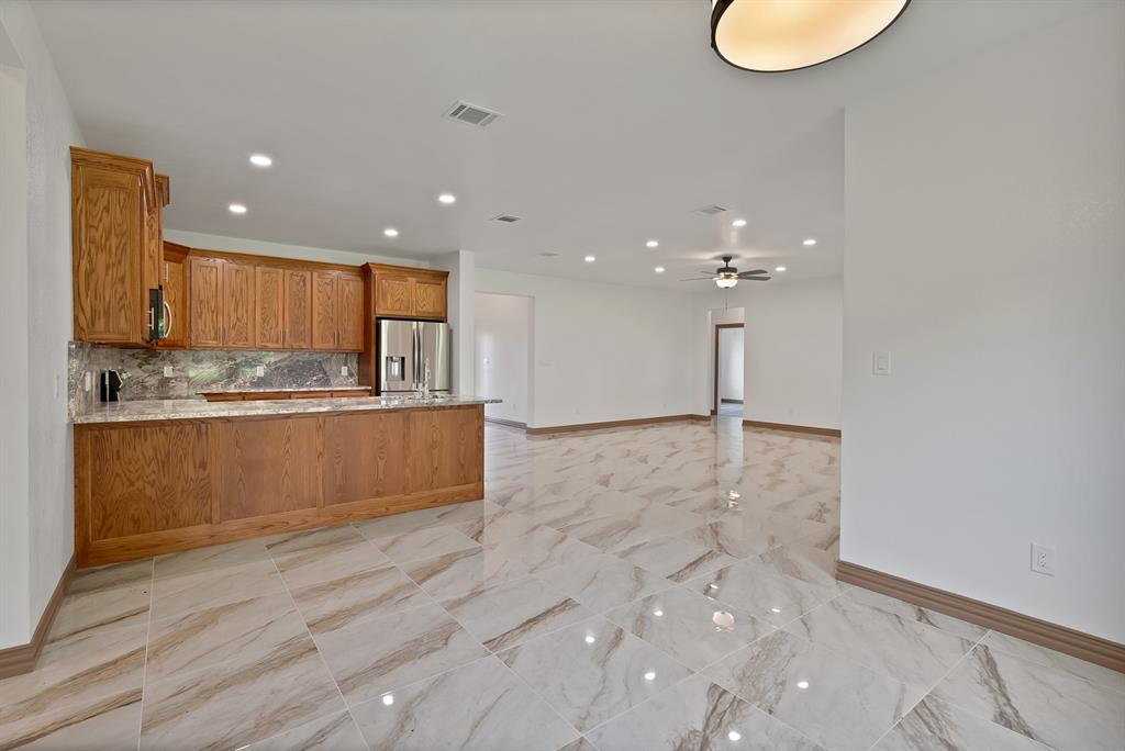 206 Hix Road Cleburne, TX 76031 - Photo 35 of 40 Kitchen featuring brown cabinets, tasteful backsplash, light stone countertops, a peninsula, and stainless steel fridge with ice dispenser