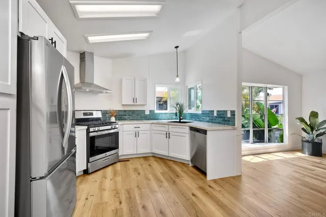 a kitchen with granite countertop a refrigerator a stove a sink and white cabinets with wooden floor