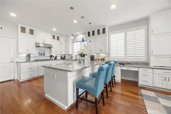 a kitchen with stainless steel appliances granite countertop a stove top oven a sink dishwasher and white cabinets with wooden floor