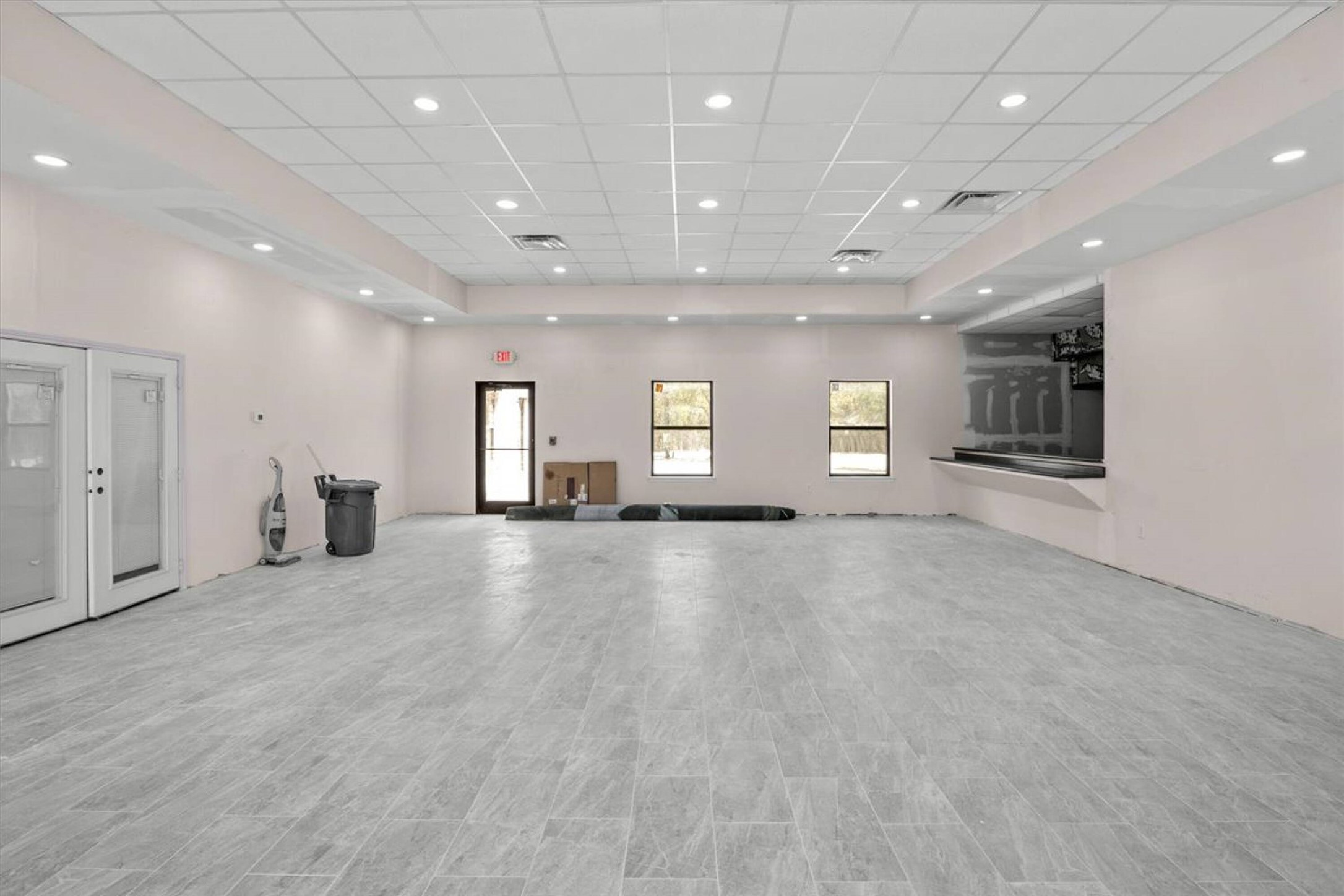 375 King Rea Spur Georgetown, TX 78633 - Photo 15 of 29 Spacious interior featuring a drop ceiling with recessed lighting, wide plank tile flooring, multiple windows, double glass-paneled entry doors, and a built-in service counter